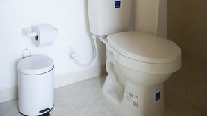 Un baño con inodoro, cubo de basura, ducha y lavamanos.