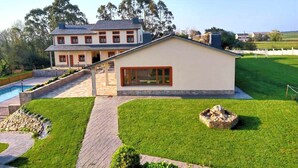 A two-story house with a swimming pool, a well-maintained lawn, and a stone feature in the yard.