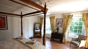 Un lit à baldaquin en bois, une chaise, une commode et une fenêtre avec des rideaux.