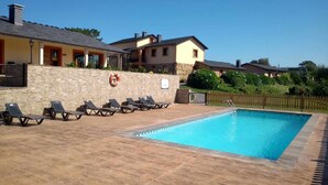 Une piscine avec des chaises longues et une bouée de sauvetage fixée à un mur de pierre, le tout entouré de maisons.