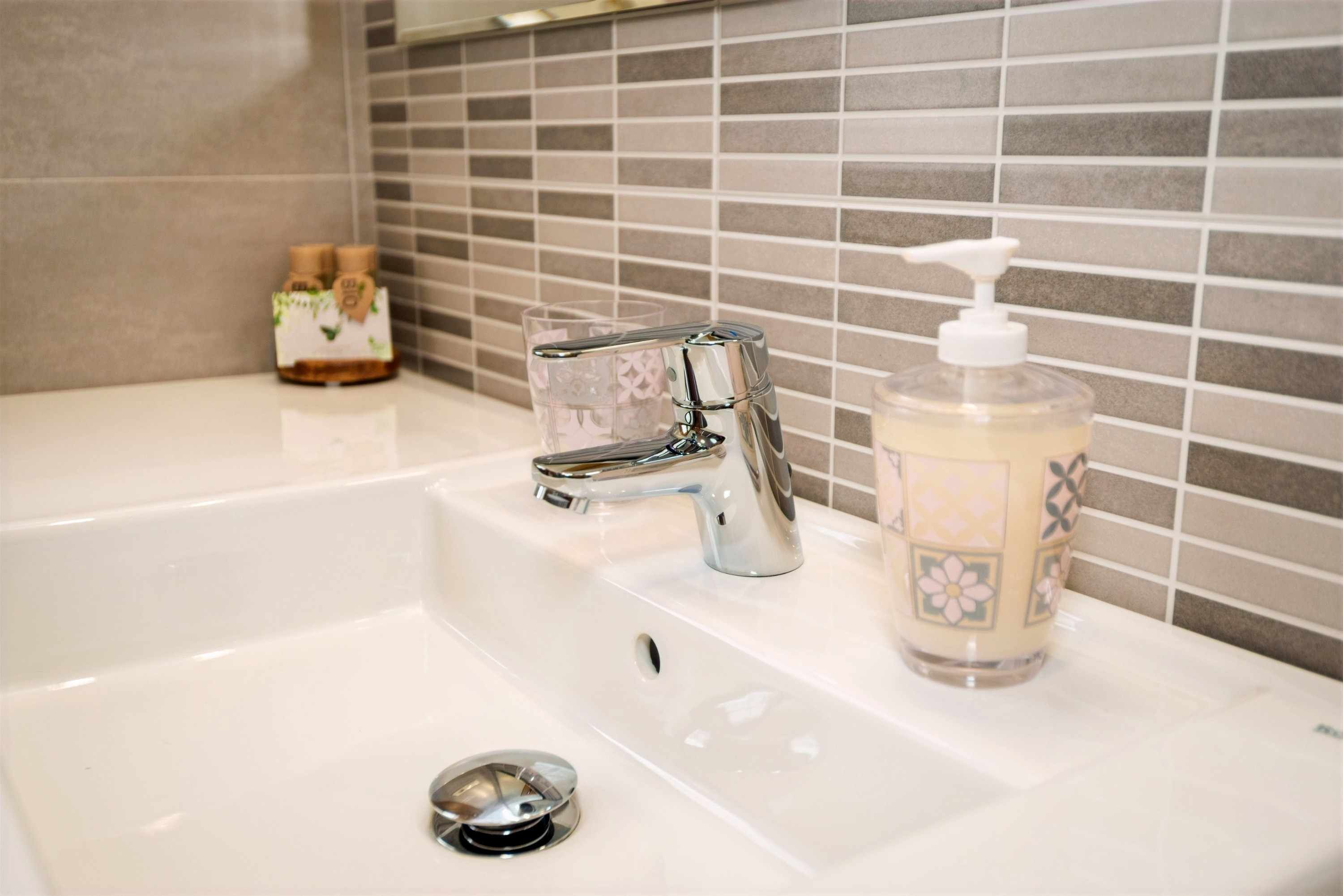A bathroom sink with a chrome faucet, a soap dispenser, and a glass.