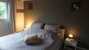 Un dormitorio con una cama, dos mesitas de noche, un buró, un ventanal con cortinas y decoración en la pared.