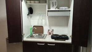 Una kitchenette compacta con un lavamanos, dos hervidores eléctricos, un escurreplatos y una pequeña encimera.