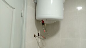 Calentador de agua blanco fijado a una pared de azulejos, conectado a una puerta blanca con pomo.