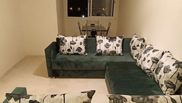 Un sofá verde con cojines estampados, una mesa de comedor con sillas, y una ventana con vistas al cielo nocturno.