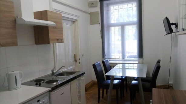 A compact kitchen with a washing machine, a dining table with chairs, and a window with blinds. - Raisa Apartments PR4 (Pressbaum)