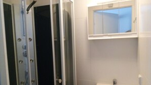 A bathroom with a glass shower enclosure, a white sink, and a mirror above the sink. - Raisa Apartments PR4 (Pressbaum)