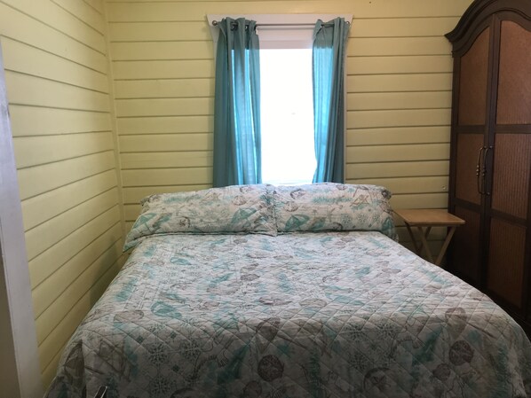 A bedroom with a bed, a window with curtains, and a wooden cabinet.