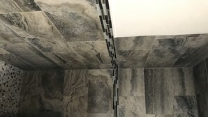 Un baño con baldosas de mármol grandes y rectangulares y una columna central con diseño de mosaico.