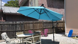 Un patio al aire libre con una mesa, sillas, un paraguas azul y una valla de madera.