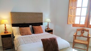 Una camera da letto ordinata con un letto grande, due comodini con lampade, una sedia di legno e una finestra con persiane in legno.