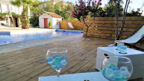 Area piscina con pavimento in legno, due sdraio e un tavolo con una ciotola di olive e bicchieri d'acqua.