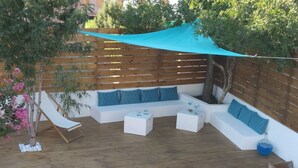 Un'area patio con un divano bianco, due tavolini bianchi, un pontile in legno e una piscina blu.