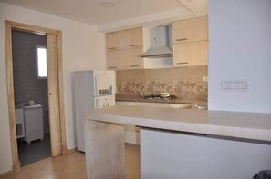 Une cuisine dotée d’un îlot central, de meubles blancs, d’une cuisinière à gaz et d’un réfrigérateur.