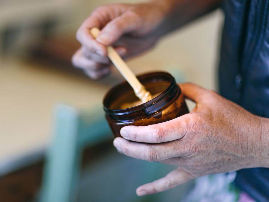A person holding a jar with a wooden spoon inside, likely containing a food item.