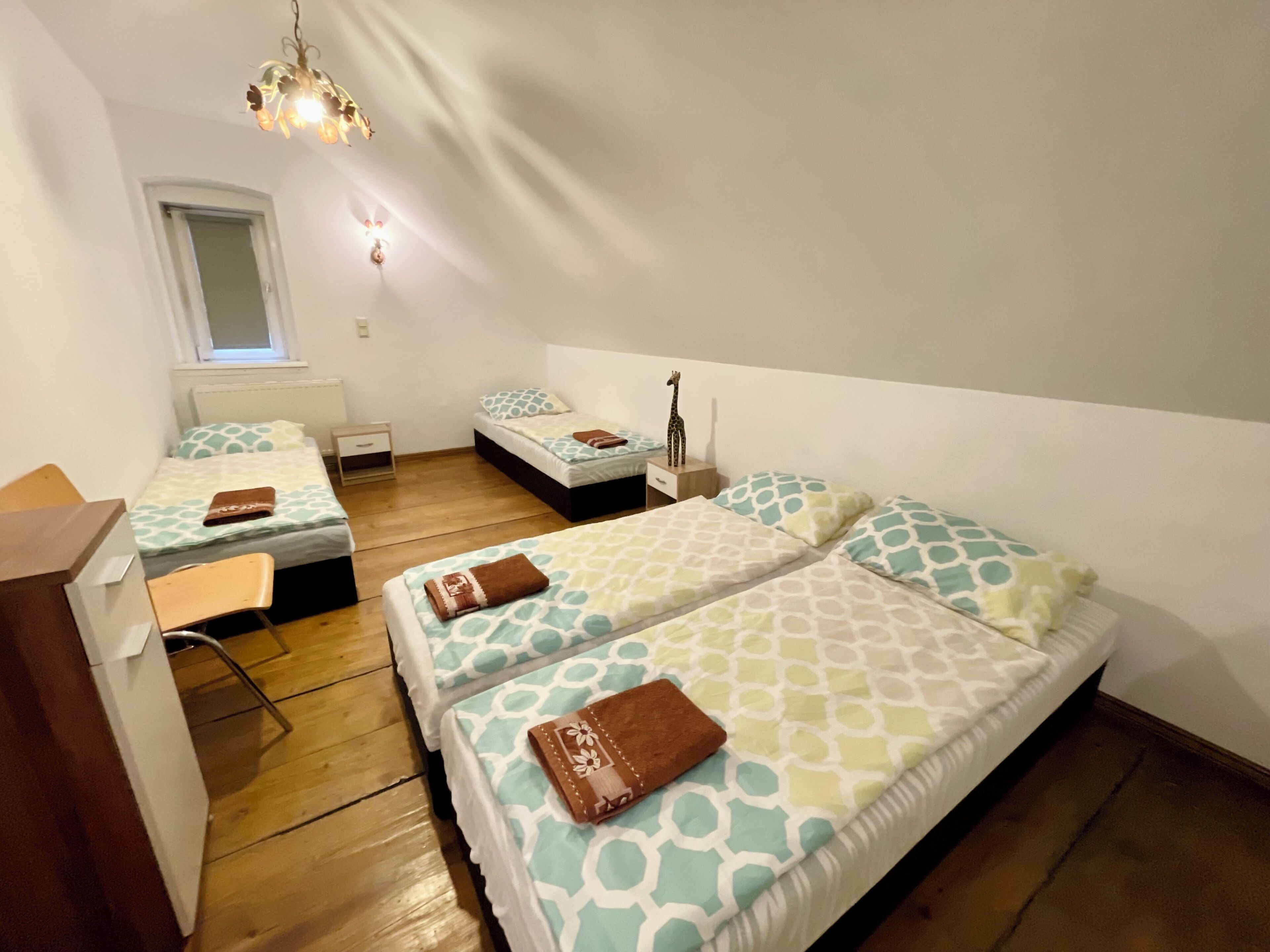 A room with two beds, a desk, a chair, a small table, and a window.