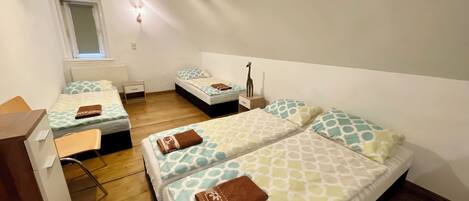 Quarto com duas camas, uma escrivaninha, uma cadeira, uma mesinha e uma janela.