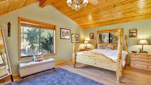 A bedroom with a wooden ceiling, a large bed, a bench, and a window with a view of trees. - Knotty AND Nice #177 (Big Bear Lake)