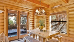 A wooden cabin interior with a dining table, benches, a chandelier, and a large window. - Knotty AND Nice #177 (Big Bear Lake)