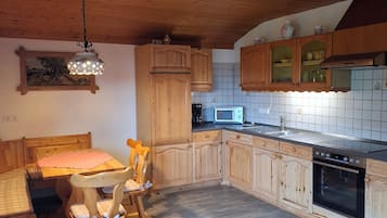 Eine Küche mit Holzausstattung, einem Esstisch mit Stühlen, einer Mikrowelle und einem Einbauofen.