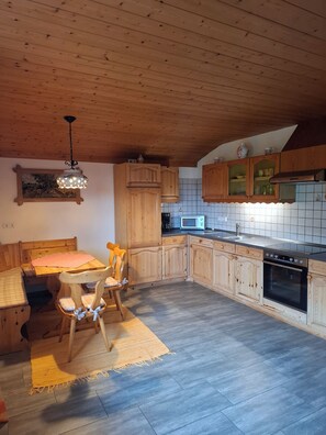 Eine Küche mit Holzausstattung, einem Esstisch mit Stühlen, einer Mikrowelle und einem Einbauofen.