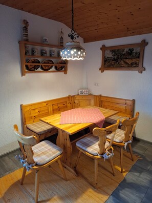 A wooden dining area with a bench and chairs, a table with a pink placemat, and a hanging light fixture. - 1A Apartment TOP (Klingenbrunn)