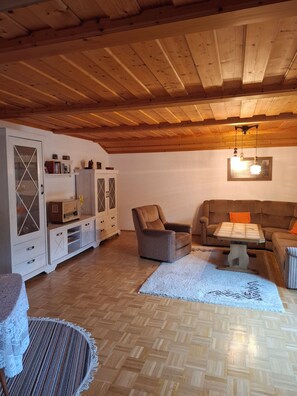 A cozy living room with wooden flooring, a sofa, a chair, a table, and a cabinet. - 1A Apartment TOP (Klingenbrunn)