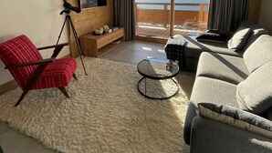 A modern living room with a large window offering a mountain view, a red chair, a grey sofa, and a small round table. - Interior comfort and divine sensations outside. New MGM apartment. (Peisey-Vallandry)