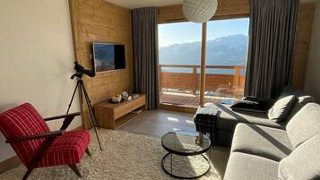 A modern living room with a large window offering a mountain view, a red chair, a grey sofa, and a small round table.