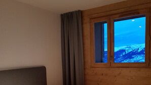 A bedroom with a single mattress, wooden walls, a window with a view of a snowy mountain, and a curtain. - Interior comfort and divine sensations outside. New MGM apartment. (Peisey-Vallandry)