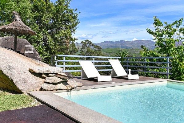 A pool with lounge chairs and a stone structure.