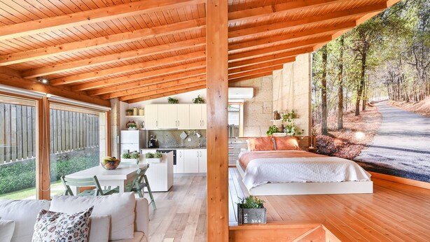 Un intérieur moderne avec des plafonds en bois, un coin repas, une cuisine et une chambre décorée d’une fresque murale.