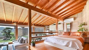 Une chambre spacieuse avec un grand lit, des poutres apparentes, un balcon et une vue sur l’extérieur.
