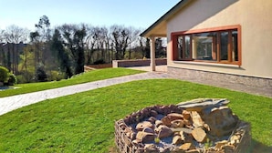 Une maison moderne avec un foyer en pierre situé dans le jardin, un chemin pavé et un patio couvert.