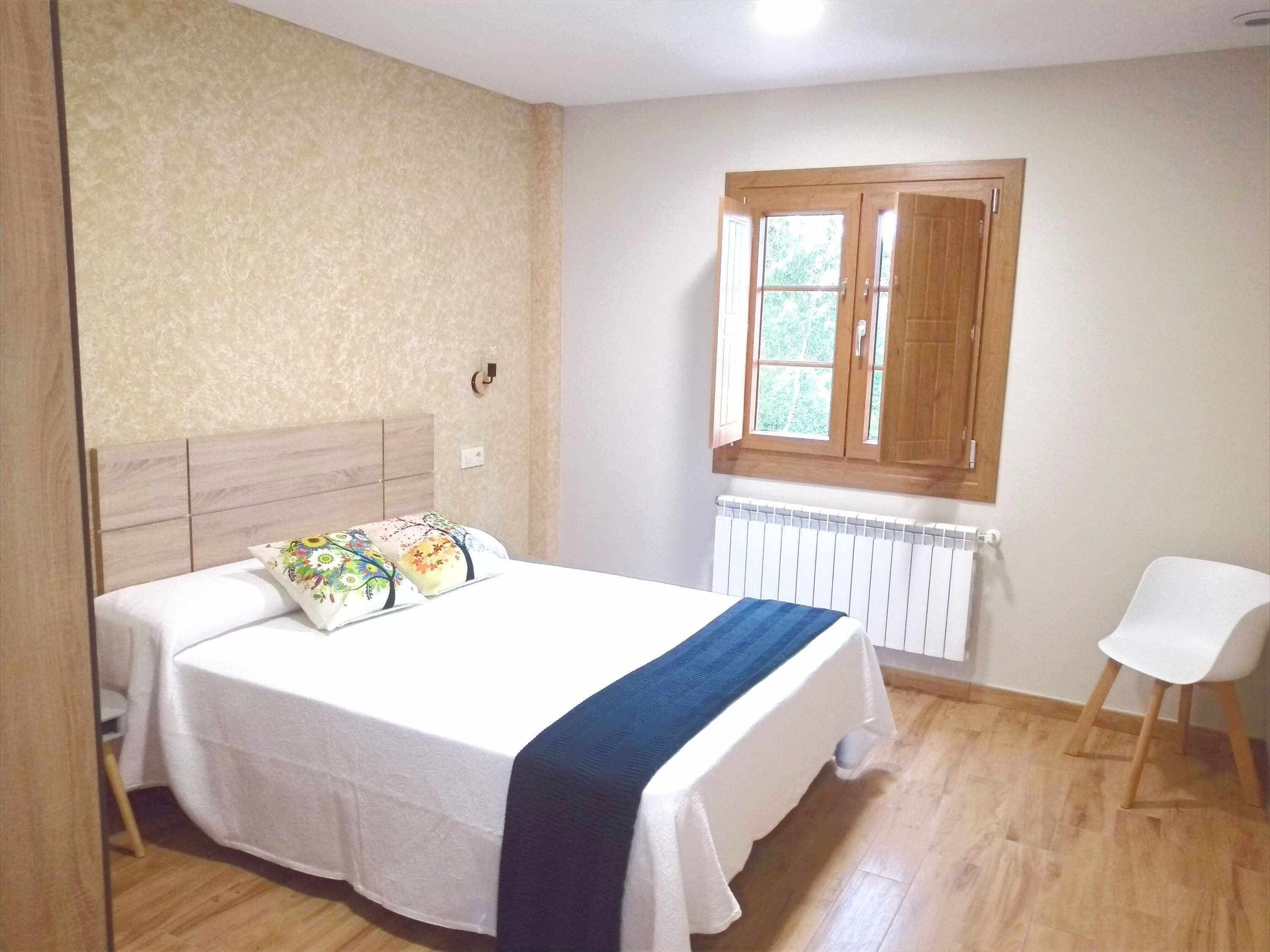 Un dormitorio con cama, ventana, radiador y una silla.