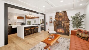 A modern living room with a stone fireplace, a kitchen with a bar area, and a cozy seating area with a sofa and a coffee table. - Vista Pines #234 (Big Bear Lake)