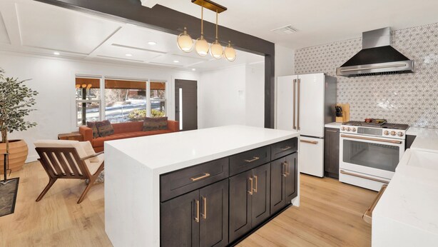 A modern kitchen with a central island, dark cabinetry, a stainless steel range hood, and a large window overlooking a snowy landscape. - Vista Pines #234 (Big Bear Lake)