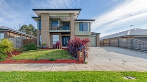 A modern two-story house with a flat roof, a balcony, and a well-maintained front yard with red mulch and green grass. - Seabreeze Haven - Wifi, Netflix, family and pet friendly beach house (Cowes)