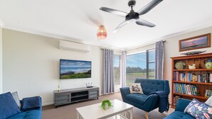 A living room with a blue sofa, a white coffee table, a bookshelf, and a television on a wall. - Seabreeze Haven - Wifi, Netflix, family and pet friendly beach house (Cowes)