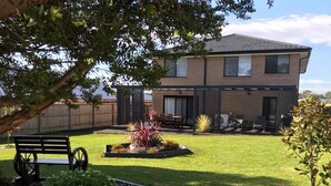 A two-story house with a brick exterior, a covered patio with outdoor furniture, and a well-maintained lawn. - Seabreeze Haven - Wifi, Netflix, family and pet friendly beach house (Cowes)