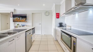 A modern kitchen with white cabinets, a stainless steel sink, a microwave, and an oven. - Seabreeze Haven - Wifi, Netflix, family and pet friendly beach house (Cowes)
