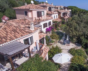 Une propriété située sur la côte, comprenant plusieurs bâtiments, un patio aménagé avec du mobilier d’extérieur et offrant une vue sur la mer.