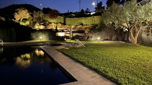 Ein Garten im Dunkeln mit Pool, Steinmauer und Sitzbereich im Freien.