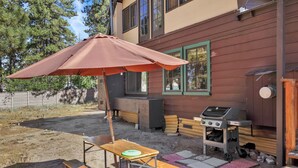 Une terrasse avec une table et un banc en bois, un barbecue et un parasol.
