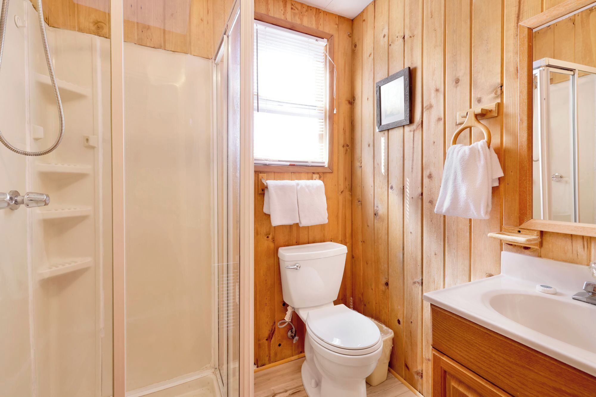Ein Badezimmer mit Holzwandverkleidung, Toilette, Waschbecken und Dusche.