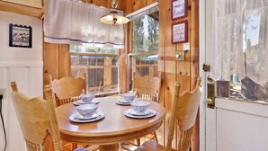 Une salle à manger en bois avec une table ronde dressée pour quatre personnes, entourée de chaises en bois.