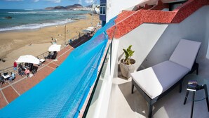 Un balcón con vistas a la playa, una silla de descanso y una planta en maceta.