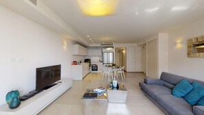 A modern living room with a flat-screen TV, a gray sofa with blue cushions, and a coffee table with books and a vase. - ❤MAMILLA 2 bdrs w. view ❤ My BEST JLM Experience ❤ (Jerusalem)