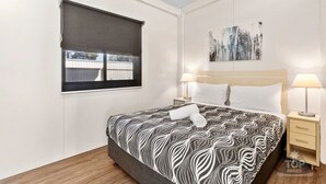 Un dormitorio con una cama grande, dos mesitas de noche con lámparas, una ventana con persiana y una obra de arte abstracta en la pared.