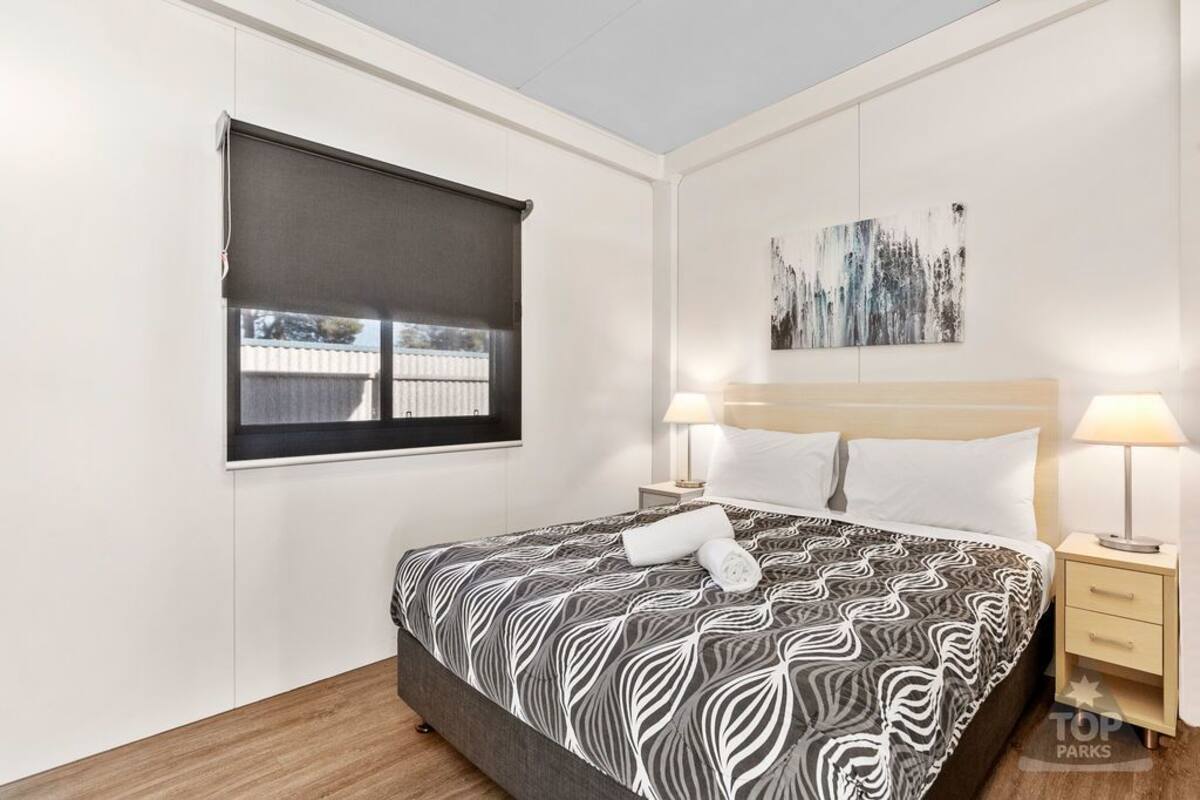 A bedroom with a large bed, two bedside tables with lamps, a window with a blind, and a piece of abstract art on the wall.